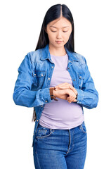 Poster - Young beautiful chinese woman pregnant expecting baby checking the time on wrist watch, relaxed and confident