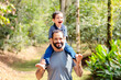 © Marcio - A joyful Brazilian father carrying his young son on his back in a lush, green forest. They are laughing and playing, highlighting a special moment of father-son bonding on Father's Day