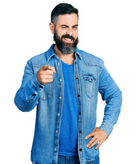 Wall Mural - Hispanic man with beard pointing with finger to camera winking looking at the camera with sexy expression, cheerful and happy face.