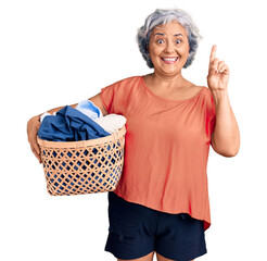 Canvas Print - Senior woman with gray hair holding laundry basket surprised with an idea or question pointing finger with happy face, number one