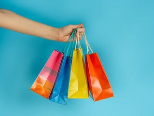 Hand holding vibrant shopping bags, isolated on blue background with ample space for text, high-resolution stock photo with soft shadows.