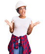 © Krakenimages.com - Young african american woman with braids wearing hardhat and builder clothes crazy and mad shouting and yelling with aggressive expression and arms raised. frustration concept.