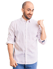 Young handsome man wearing elegant shirt smiling with happy face looking and pointing to the side with thumb up.