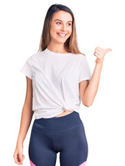 Wall Mural - Young beautiful girl wearing casual t shirt smiling with happy face looking and pointing to the side with thumb up.