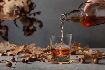 Sticker - Whiskey on a grey stone table with dried-up oak leaves.