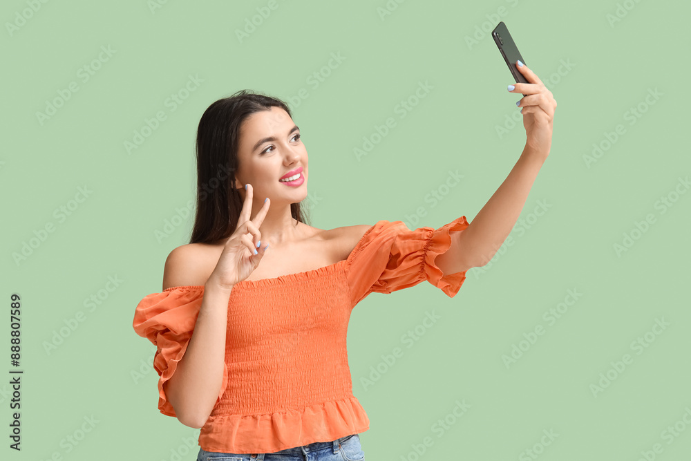 Beautiful happy young woman taking selfie on green background