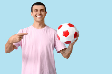 Wall Mural - Handsome young man pointing at soccer ball on blue background