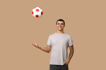 Wall Mural - Handsome young man playing with soccer ball on brown background