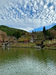 Wall Mural - Traditional Japanese village with thatched-roof houses by a tranquil lake under a partly cloudy sky