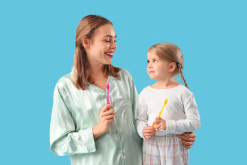 Wall Mural - Young mother and her little daughter with toothbrushes on blue background