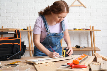 Canvas Print - Female carpenter measuring plank length with tape in workshop