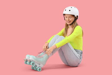 Wall Mural - Beautiful young woman in helmet and roller skates sitting against pink background