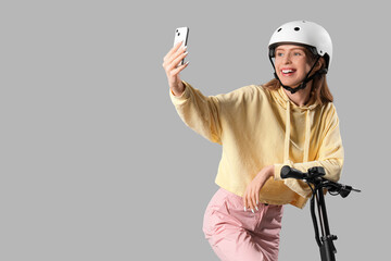 Sticker - Beautiful young woman in helmet with modern electric kick scooter taking selfie on grey background