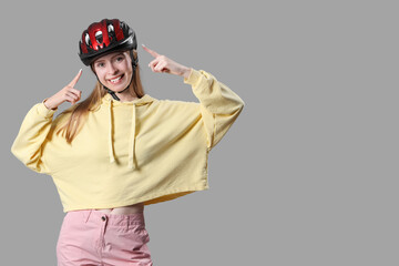 Poster - Beautiful young woman pointing at helmet on grey background