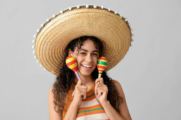 Poster - Beautiful young African-American woman in sombrero hat with maracas on grey background