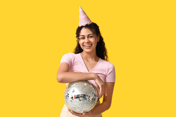 Poster - Beautiful young African-American woman in party hat with disco ball on yellow background