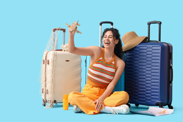 Wall Mural - Young African-American woman sitting on floor and plying with wooden airplane near suitcases on blue background