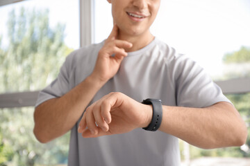 Poster - Sporty young man with smartwatch checking pulse in gym, closeup