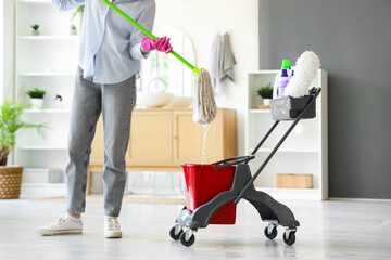 Poster - Young woman with cleaning supplies in trolley mopping floor at home, closeup