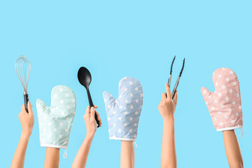 Wall Mural - Female hands with different baking utensils and mittens on blue background