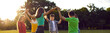 © Studio Romantic - Group of children holding hands and dancing in circle on green lawn in park on beautiful summer day. Boys and girls in colored casual clothes raise their hands walking in circle. Panoramic web banner.