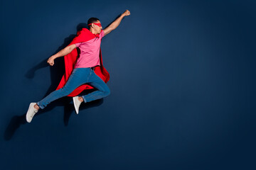 Poster - Full length body photo of young flying super guy in red face mask and cape fights against empty space isolated on dark blue color background