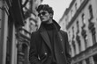 © Sergio - A man wearing sunglasses and a coat stands on a city street, black and white