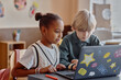 © Seventyfour - Two focused primary school children of diverse ethnic backgrounds using in-class laptop together utilizing online learning tools sitting at table