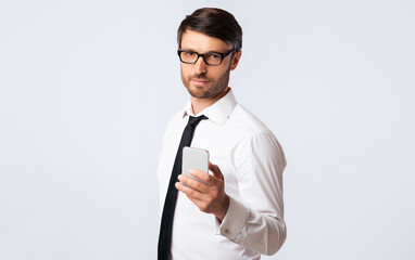 Poster - A businessman in a white shirt and black tie holds a smartphone in his hand while looking at the camera.