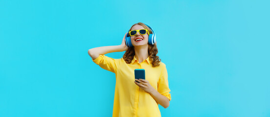 Wall Mural - Modern happy young woman listening to music with smartphone, girl smiles in headphones holding phone