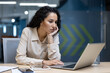 © Liubomir - Young professional woman focused on laptop at modern office. Work environment with electronic devices and paperwork. Concept of business, technology, and productivity.