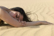 © Connect Images - A serene woman lying on a sandy beach with her head resting on her arm, eyes closed, conveying a sense of peace and relaxation.