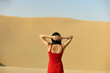© Connect Images - Woman in a red dress standing with hands clasped behind her head, gazing at a vast desert landscape.