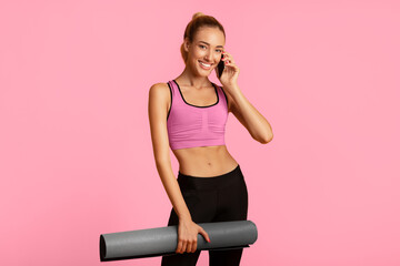 Wall Mural - Happy Lady Talking On Phone Holding Fitness Mat Smiling At Camera Standing On Yellow Background. Studio Shot