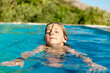 © Connect Images - Child swimming in a pool with eyes closed and a calm expression during a sunny day.