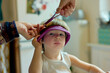 © Connect Images - A child sits patiently while an adult hand cuts their hair with scissors, a purple headband is used to keep the hair in place.