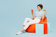 © ViDi Studio - Full body young woman wears casual clothes sit in bag chair near bags use mobile cell phone hold credit bank card shopping online isolated on plain blue background Black Friday sale buy day concept