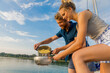 © Connect Images - A happy couple cooking pasta on a boat with a scenic lake background during sunset
