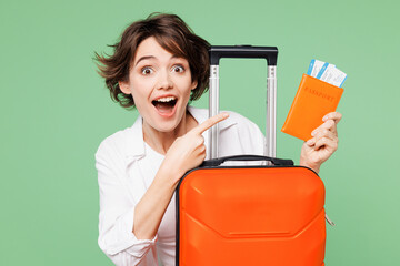 Wall Mural - Close up traveler happy woman wear casual clothes hold point on passport ticket suitcase bag isolated on plain green background Tourist travel abroad in free time rest getaway Air flight trip concept