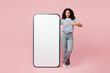 © ViDi Studio - Full body little kid teen girl wear blue t-shirt casual clothes point finger on big huge blank screen mobile cell phone smartphone with area isolated on plain pastel pink background Childhood concept