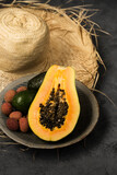 Two avocados, half a papaya and lychee berries on a clay plate near the straw hat