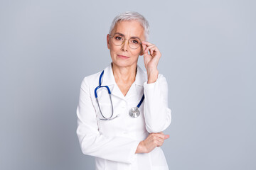 Poster - Photo portrait of attractive senior woman hospital doctor worker touch specs dressed white robe uniform isolated on gray color background