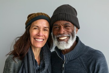 Wall Mural - Portrait of a happy mixed race couple in their 60s donning a warm wool beanie in bare monochromatic room