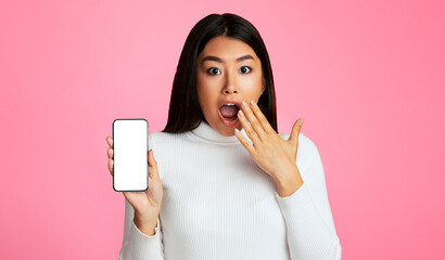 Poster - Asian young woman with long dark hair, wearing a white sweater, standing in front of a pink background. She is holding a smartphone with a blank screen in her left hand and covering her mouth