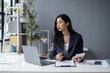 © apichat - A woman is sitting at a desk with a laptop and a calculator