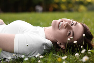 Wall Mural - Portrait of smiling woman lying on grass and flowers. Spring vibes