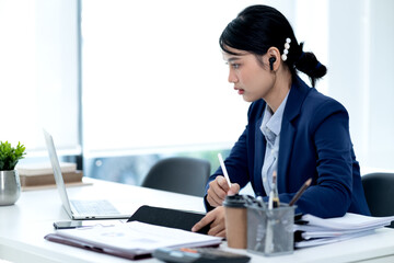 Poster - young business woman is writing notes on the data she is viewing on the notebook