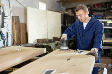 Wall Mural - Man carries out preparatory work with wooden board, grinds surface with hand-held device and levels surface of material