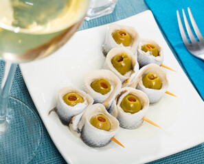 Sticker - Appetizing pickled herring rolls with stuffed olives served on white plate..