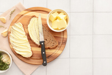 Wall Mural - Wooden board with bread slices, garlic and bowl of fresh butter on white tile background